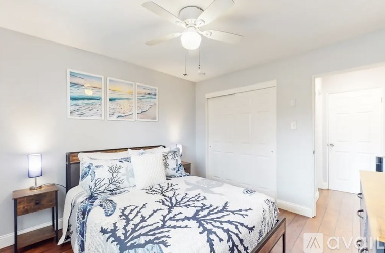 A bedroom with a bed, a ceiling fan, and a painting on the wall.