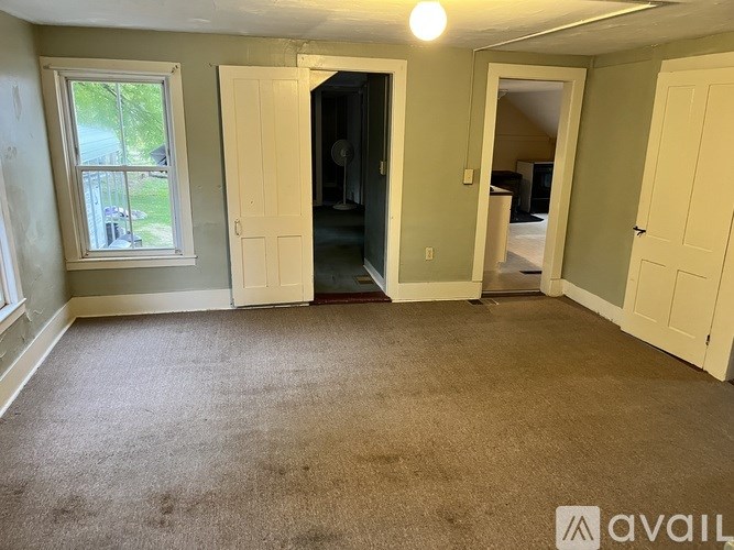 A room with carpeted floor and a window with a view of a lawn and trees.