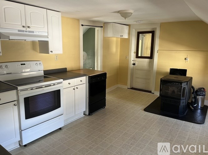 A kitchen with white appliances and cabinets, a black oven, and a tiled floor.