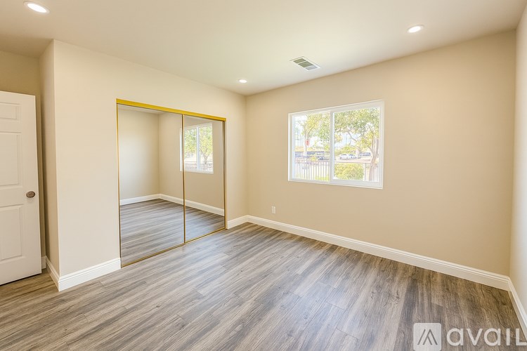 A room with a white door, a window, and a wooden floor.