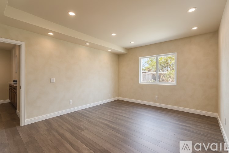 A spacious room with wooden flooring and a window showing trees outside.
