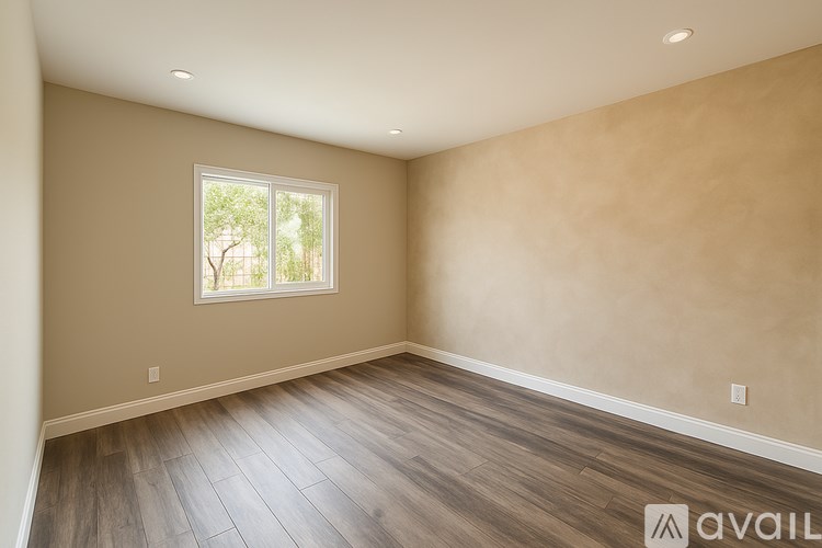 A room with wooden flooring and a window showing trees outside.