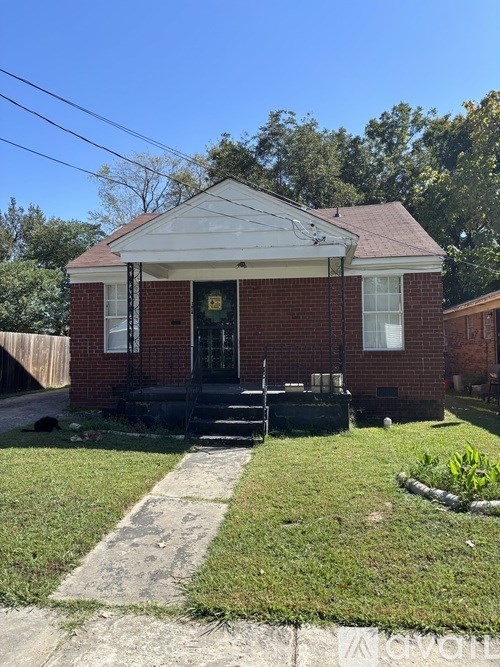 A small red brick house with a porch and a front yard.