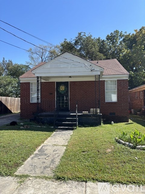 A small red brick house with a porch and a front yard.