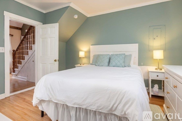 A bedroom with a white bed and a white dresser with a lamp on it.