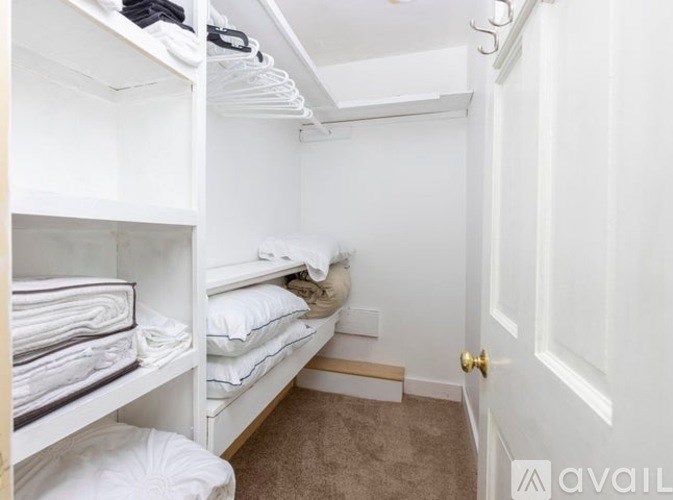 A white room with a bed and towels on the shelf.