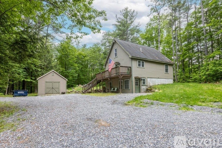 A house with a flag on the balcony is surrounded by trees.