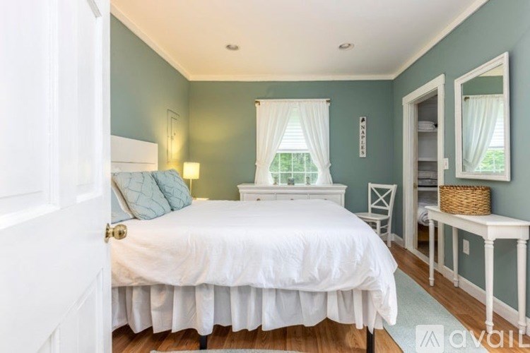 A bedroom with a white bed and a window with white curtains.