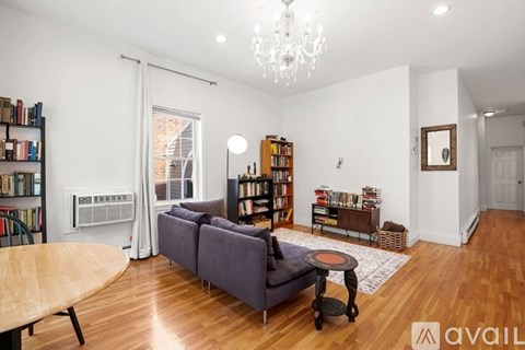 A living room with a grey couch, a wooden table, a chandelier, and a bookshelf filled with books.