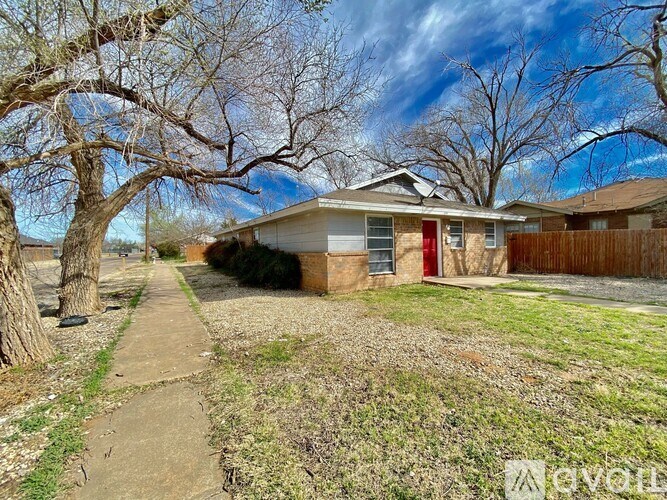 A house with a red door is surrounded by a fence and trees.