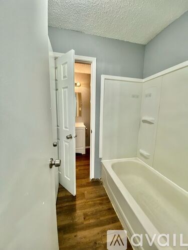 A white bathroom with a bathtub and a door open to another room.
