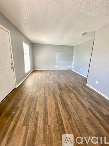 A room with wooden flooring and a door on the left.
