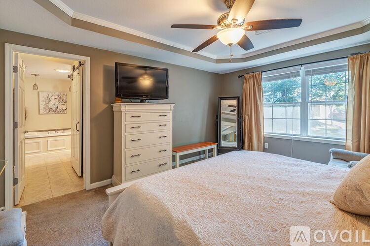 A bedroom with a large bed, a television, and a window with curtains.