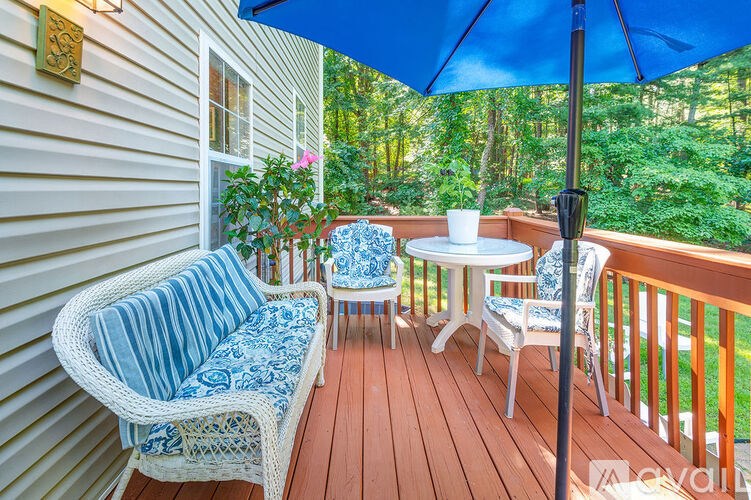 A blue umbrella is on a wooden deck with a white table and chairs.
