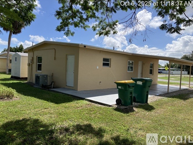 A beige house with a green trash can in front of it.