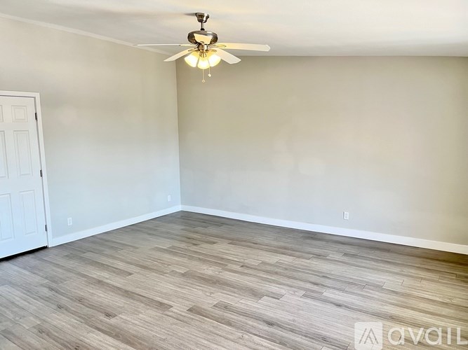 A room with a ceiling fan and light fixture, and a wooden floor.