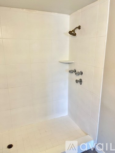 A white tiled shower with a shower head and hand held shower.