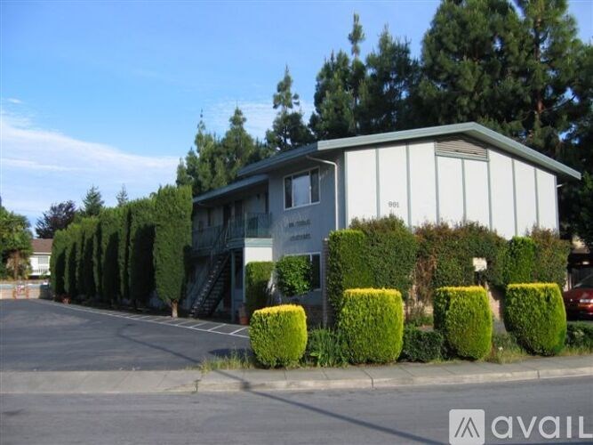 A building with a grey roof and white walls is surrounded by green bushes.