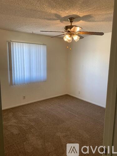 A room with a carpeted floor, a ceiling fan, and a window with blinds.