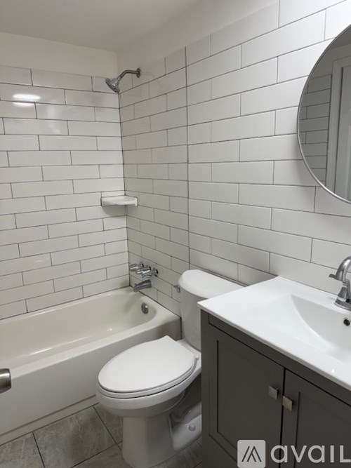 A white toilet sits next to a bathtub in a bathroom with white tiles.