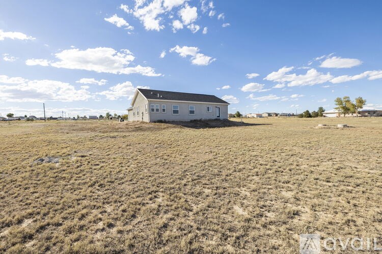 A white house sits in a dry, grassy field under a blue sky with clouds.