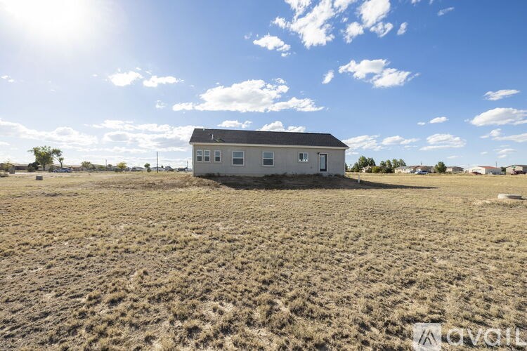 A small house sits in a dry, grassy field under a blue sky with clouds.
