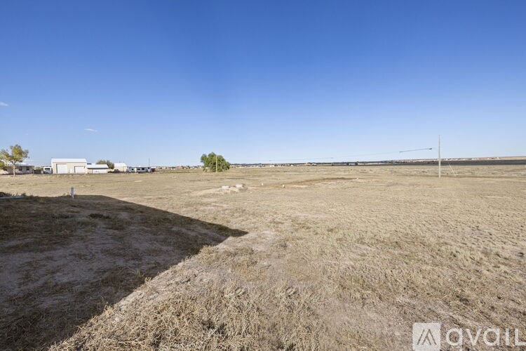 A barren field with a building and a wind turbine in the distance.