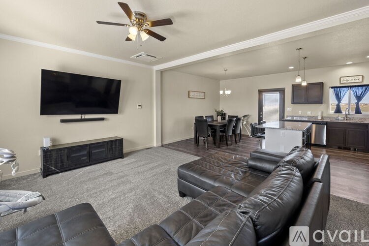 A living room with a black leather couch and a flat screen TV mounted on the wall.