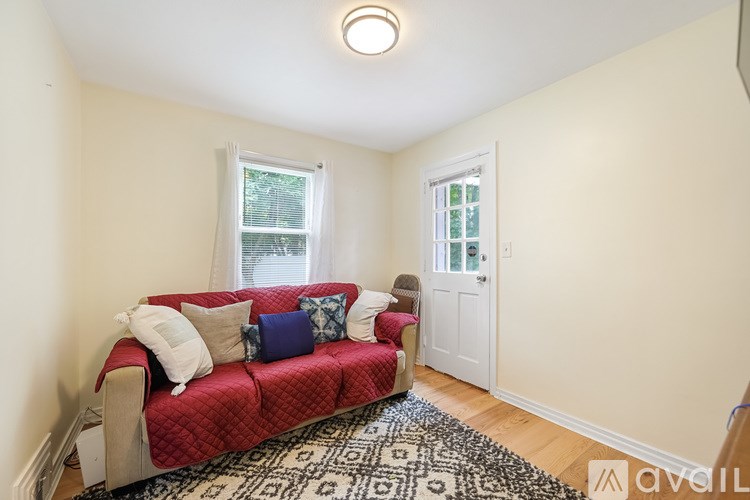 A red couch with white and blue pillows sits in a room with a window and a door.