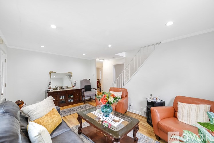 A living room with a grey couch, a brown leather couch, a glass coffee table, and a staircase in the background.