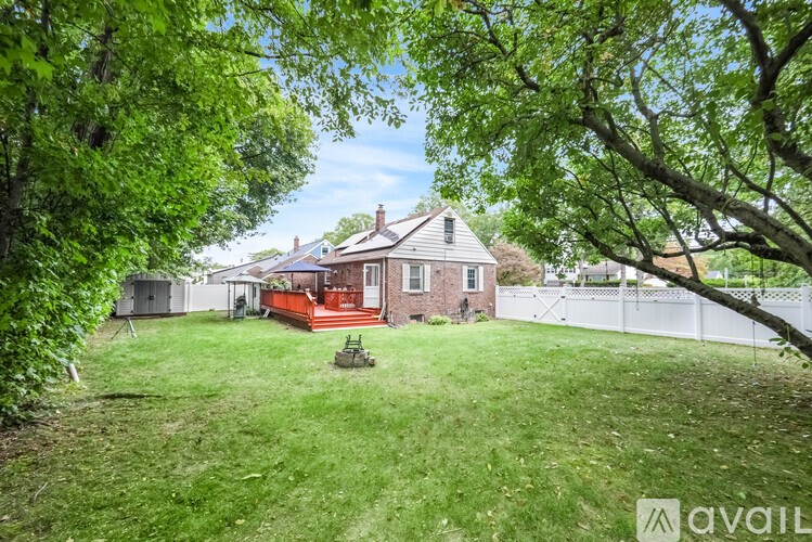 A house with a red deck is surrounded by a white fence and green trees.