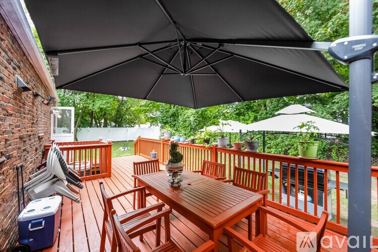 A wooden table and chairs are set up on a deck under a large black umbrella.