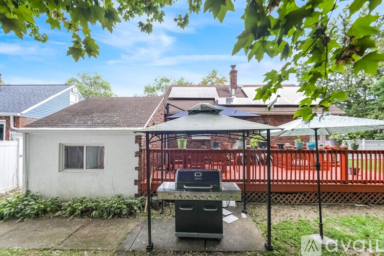 A barbecue grill is set up on a patio with a white house and a red fence in the background.