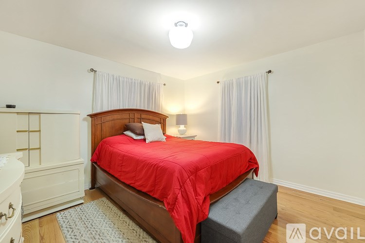 A bedroom with a red bedspread and a white nightstand.