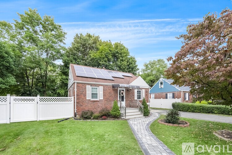 A house with a white picket fence and a brick exterior with a solar panel on the roof.