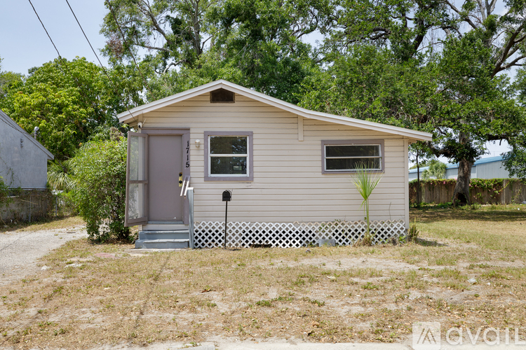 A small house with a grey door and a window is surrounded by a white picket fence.