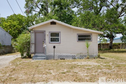 A small house with a grey door and a window is surrounded by a white picket fence.