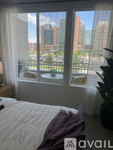 A bedroom with a large window overlooking a parking lot and buildings.