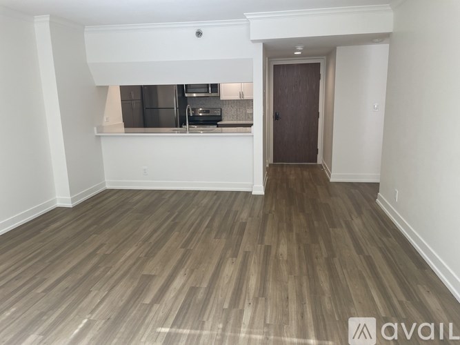 A room with wooden flooring and a kitchen area in the background.