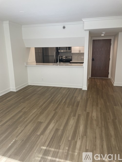A room with wooden flooring and a kitchen area in the background.