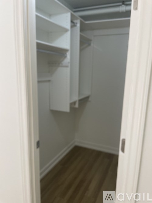 A white door is open to a small, empty room with wood flooring.