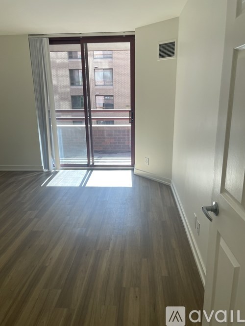 A room with wooden floors and a sliding glass door leading to a balcony.