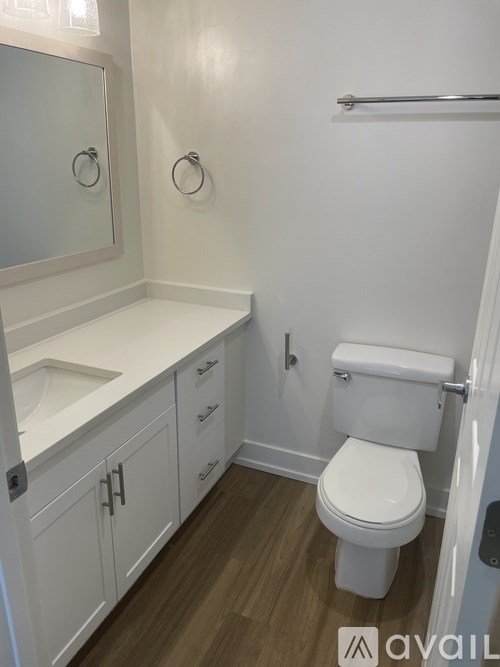 A white toilet in a small bathroom with a white sink and a towel bar.