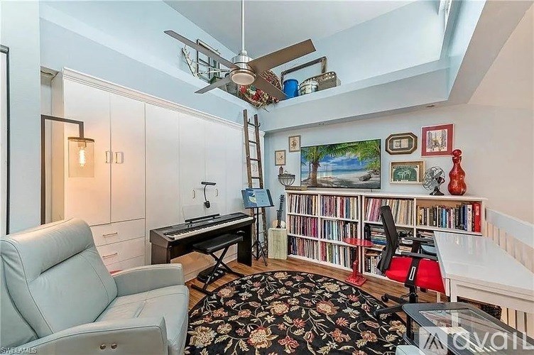 A living room with a grey sofa, a black and white rug, a desk with a computer, a bookshelf with books, and a painting on the wall.