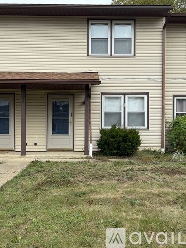 A house with a brown roof and beige siding with a small bush in front.
