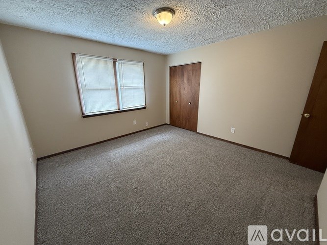 A room with a carpeted floor, a window with blinds, a door, and a ceiling light fixture.