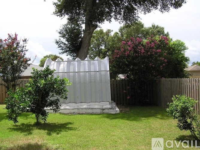 A garden with a large tree, a fence, and a small building.