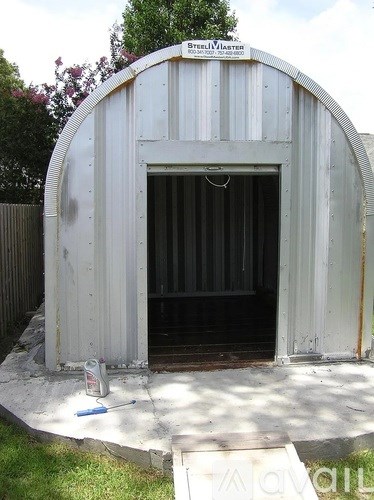 A white metal building with a door open and a can of paint on the ground.