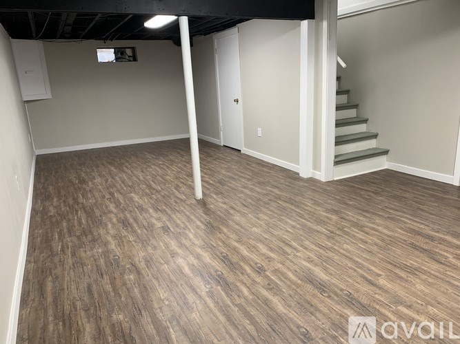 A room with wooden flooring and a staircase in the background.