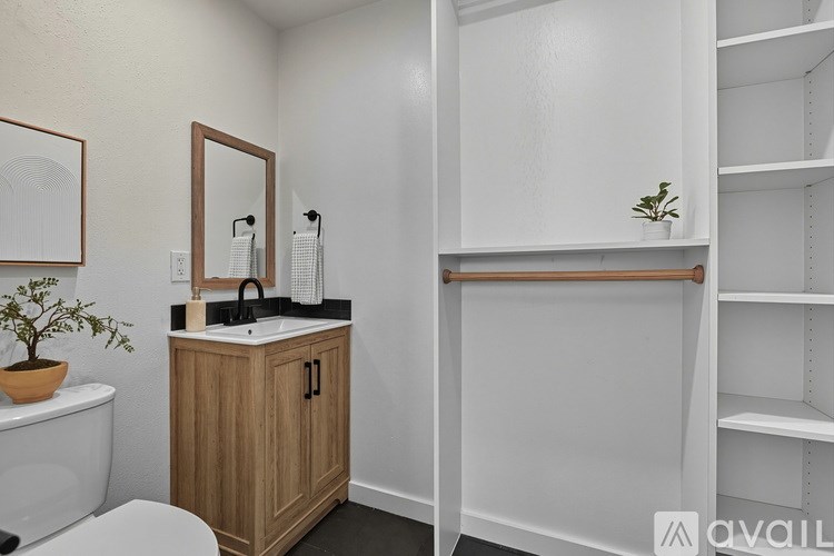 A bathroom with a white toilet, a wooden cabinet with a mirror above it, and a white sink with a plant on top.